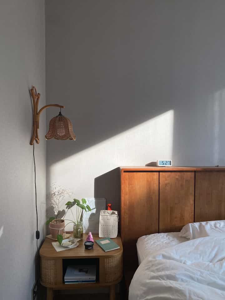 Cozy bedroom in soft white and wood tones featuring rattan wall lamp and nightstand with natural ambiance