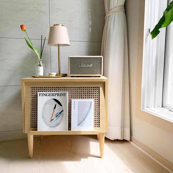 Bright wood tone and beige living room corner featuring a rattan storage cabinet with a table lamp and Bluetooth speaker on top, creating a cozy atmosphere