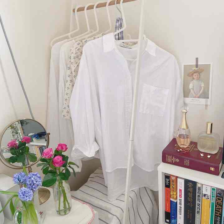 柔らかい白のトーンの寝室の一角、服掛けに白いシャツが掛かり、鏡と花瓶が配された整った空間