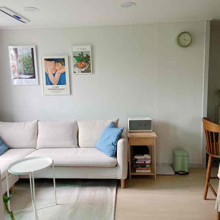 白い壁と木目調家具が配置されたモダンでナチュラルなリビング、ベージュのソファとブルートゥーススピーカーが落ち着いた雰囲気を演出する空間