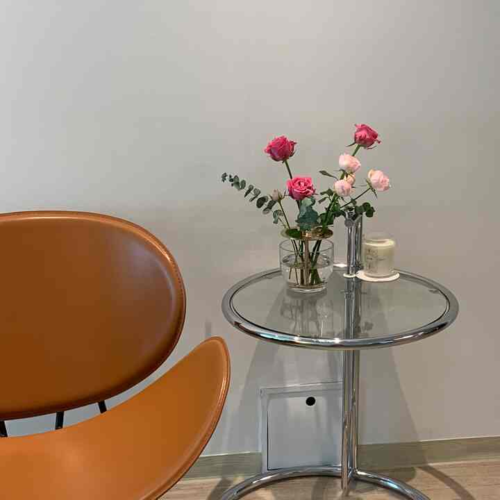 明るくシンプルなリビング、オレンジのミッドセンチュリーモダンアームチェアとガラスの花瓶が置かれたクロームのサイドテーブル