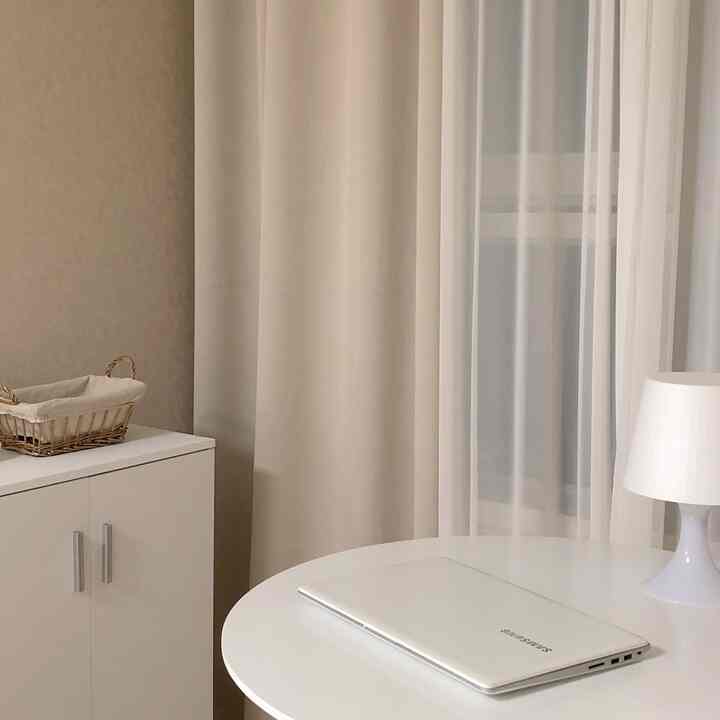 白とベージュのトーンの一人暮らしワンルーム、丸いダイニングテーブルとテーブルランプ、収納が配置された落ち着いたシンプルな自宅