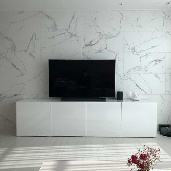 白を基調としたモダンなリビング、白いテレビ台と大型テレビ、サウンドバーが配置された清潔感のあるインテリア