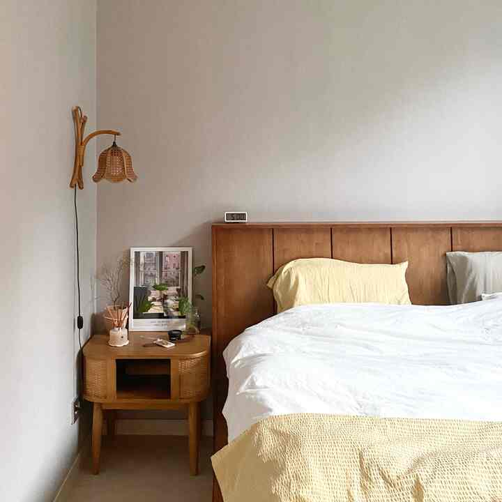 A natural-toned bedroom featuring white and wood tones, with a nightstand, picture frame, and lamp arranged on the side