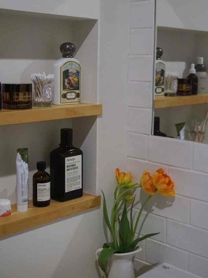 White walls and tiles bathroom niche with wooden shelves and vibrant orange tulips in a vase