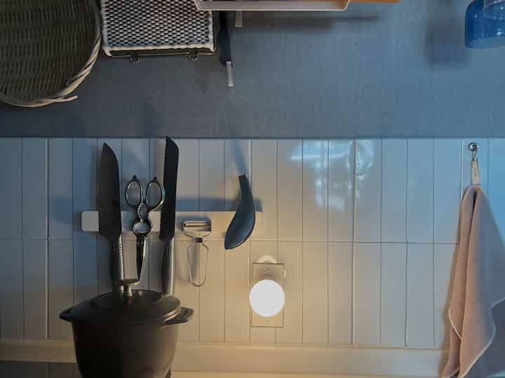 白いタイル壁にシルバーのステンレス製マグネットパネル、包丁や調理器具が配置されたモダンなキッチンインテリア