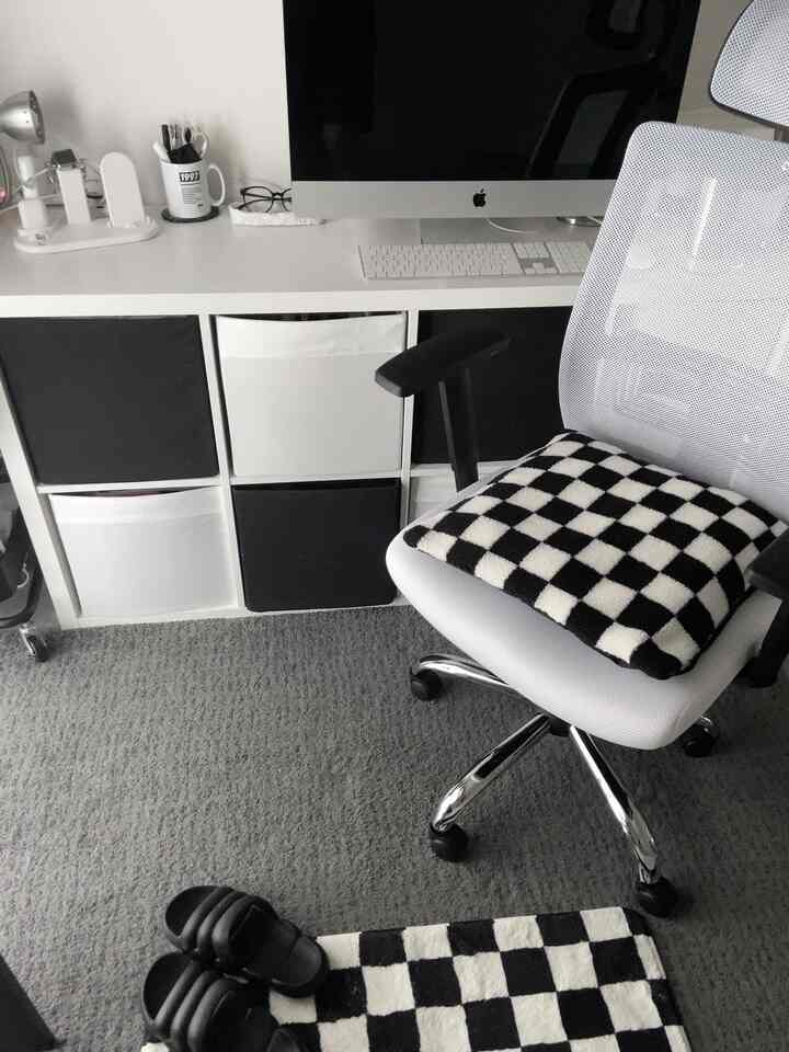 ホワイトとブラックの色調によるコンパクトなホームオフィス空間。整ったデスクとチェッカーボード柄のクッションとラグを配したモダンなワークスペース。