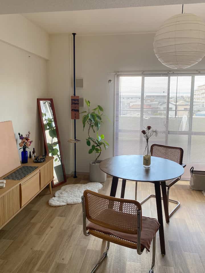 明るいホワイトの壁と木目調家具が配置されたダイニング、丸テーブルと椅子、観葉植物があるナチュラルな空間