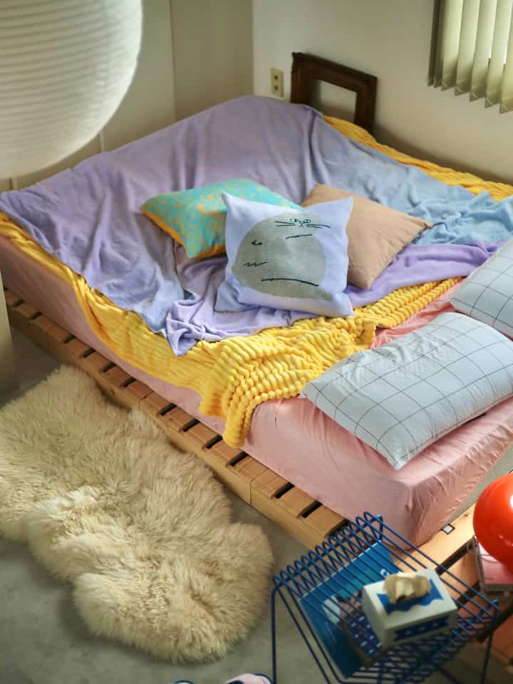 A bedroom with yellow and lavender tones, featuring a natural wood bed and cat-illustrated cushions for a warm atmosphere