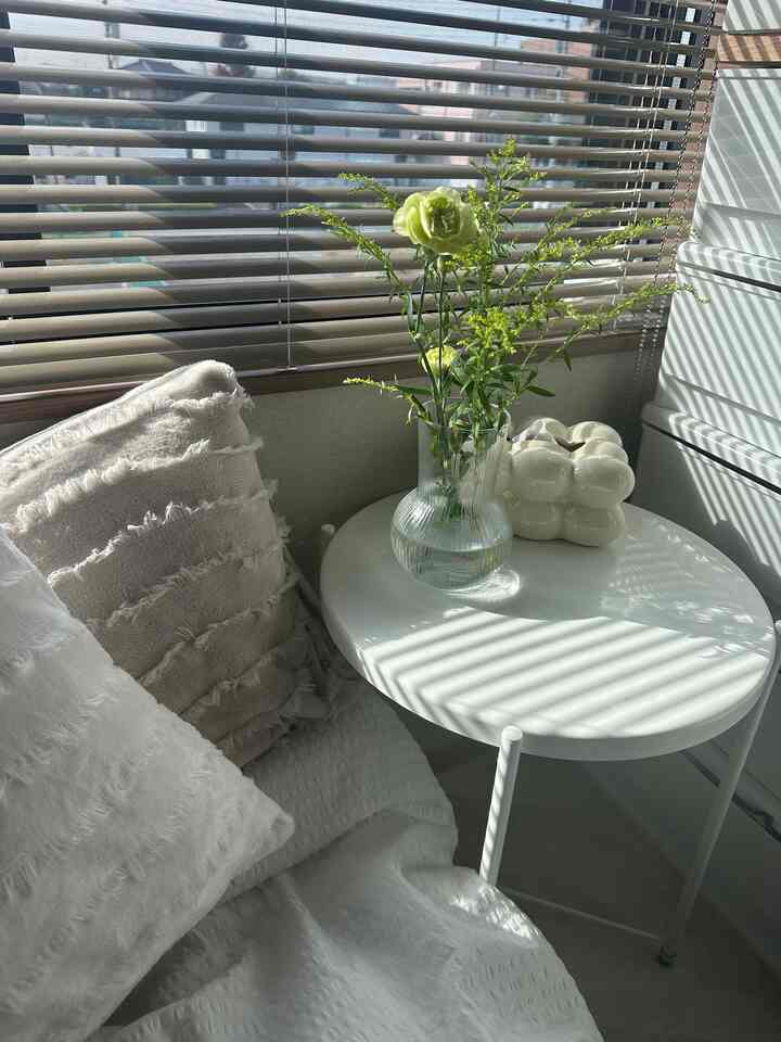白とナチュラルカラーのバルコニー空間、花瓶とクッションが配置された居心地の良い日差しの差し込むインテリア