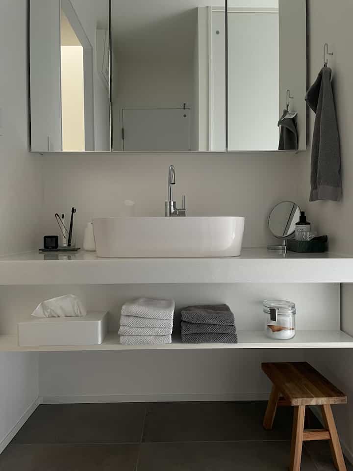 ホワイトとグレーの色調が映える洗面所、シンプルで整然としたタオルとスツールが配置されたミニマルな空間