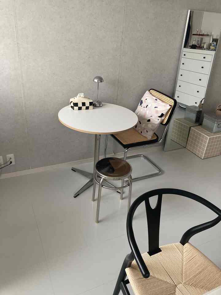 白を基調とした床と壁のコンパクトな部屋に、丸いダイニングテーブルと様々な椅子が配置されたミニマルでモダンな印象的な空間