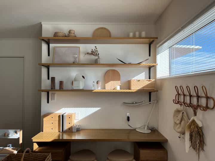 白い壁と木目調の家具が調和するホームオフィス空間、棚と机に収納アイテムが整頓されたシンプルでナチュラルな雰囲気のインテリア