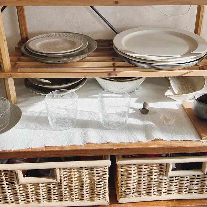 Natural toned kitchen shelf featuring plates, clear glasses, and dark wooden baskets organized neatly