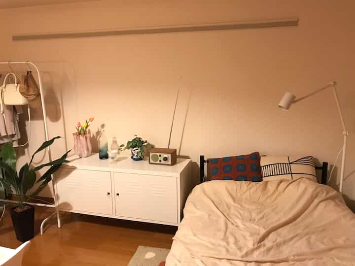 暖かいベージュと白の色調の寝室、ナイトテーブルとフロアランプが配置された一人暮らしの居心地の良い空間