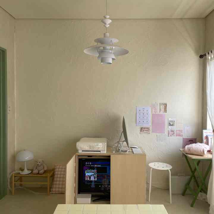 Small home office space harmonizing natural beige tones with white, featuring a desk, stool, printer, and pink posters adorning the wall, creating a cozy work atmosphere
