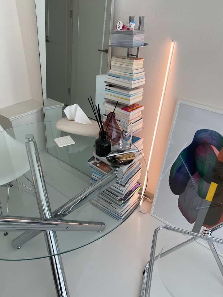 シルバーと白のトーンの狭い部屋、本棚とガラステーブルが配置されたモダンで清潔感のあるインテリア