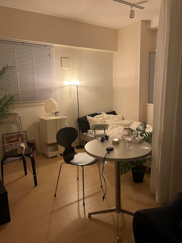 白と茶色のトーンの小さな寝室、丸テーブルとフロアランプが配置された雰囲気のあるインテリア