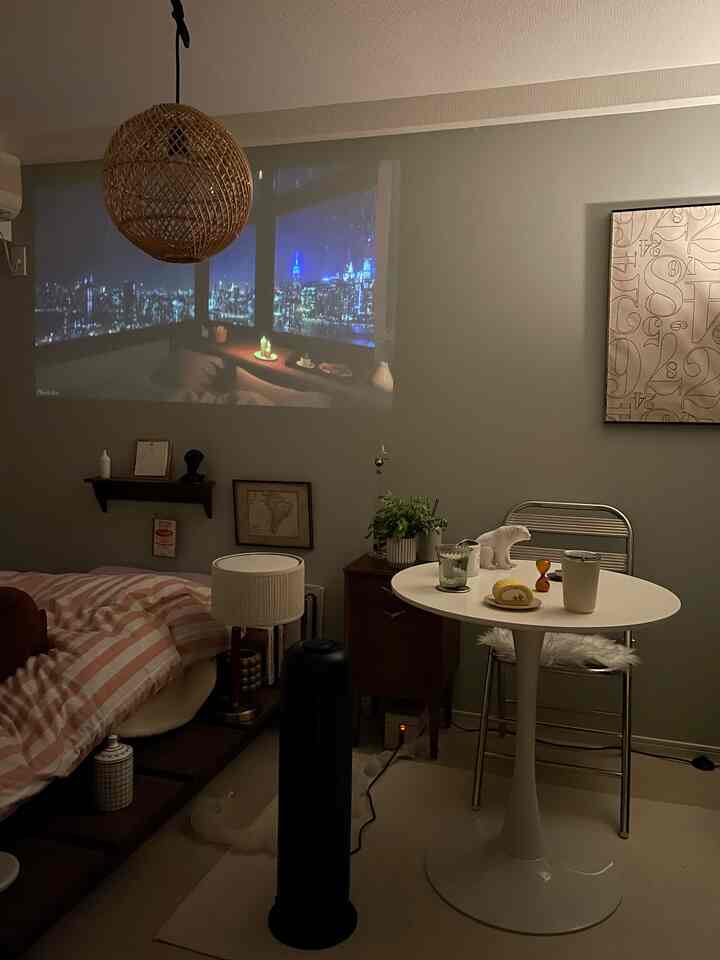 A cozy small bedroom in white and brown tones featuring a round dining table and a projector screen creating a warm atmosphere