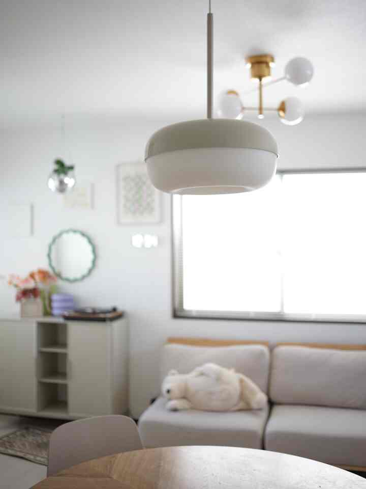 明るく爽やかなベージュと白のトーンのリビング・ダイニング、ベージュのソファと丸いダイニングテーブル上のペンダントライトが配置された、自然でシンプルな雰囲気のインテリア