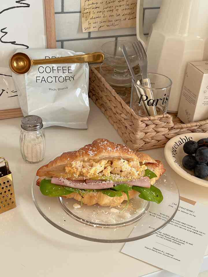 白と茶色のトーンのキッチン、クロワッサンサンドとコーヒー用品が置かれた清潔なダイニングテーブル。