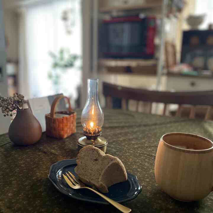 Classic wood-tone dining table with lit oil lamp and a slice of chiffon cake in a cozy kitchen space