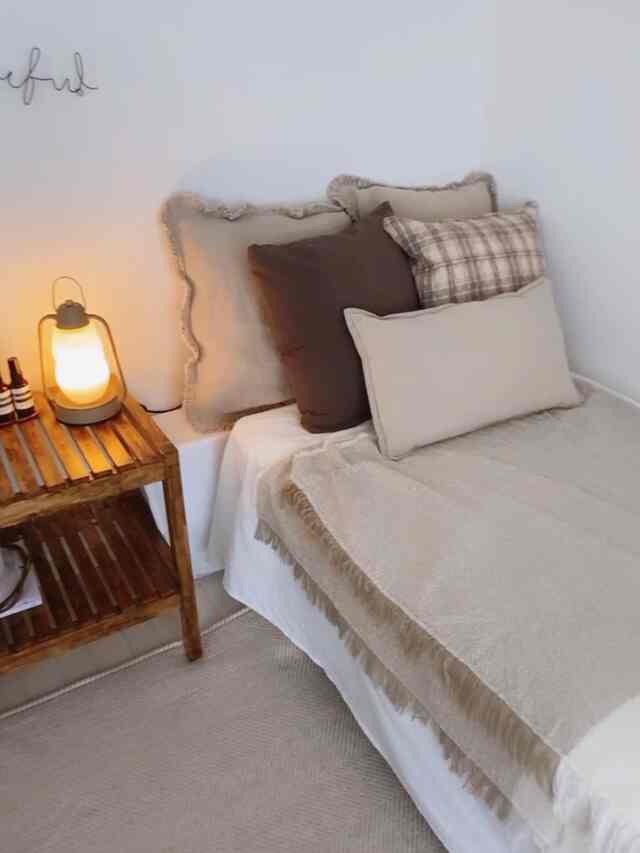 ベージュとブラウンの寝室、枕とスローを配したベッドと木製のサイドテーブルが置かれた、自然な雰囲気のある印象的な空間