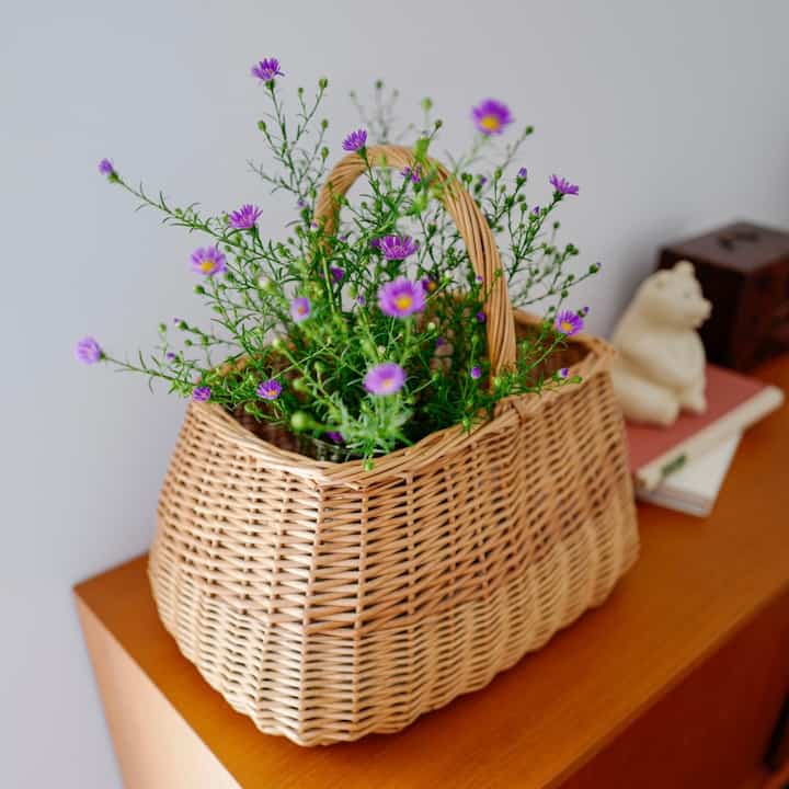 茶色い木のテーブルに置かれたナチュラルなバスケットと紫色の小さな花がある雰囲気のあるインテリア