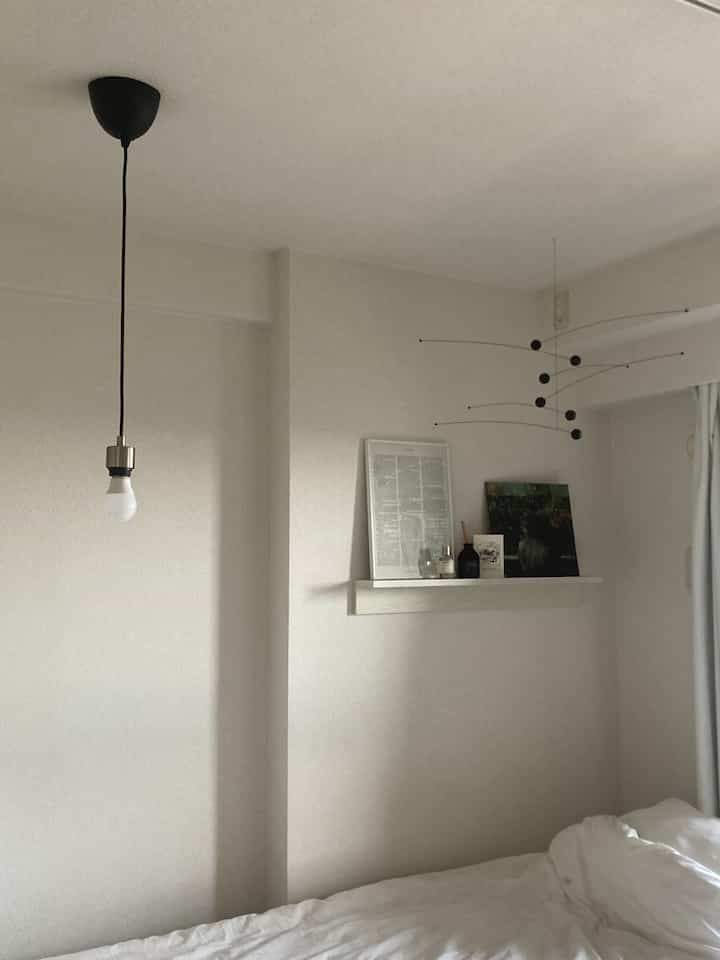 白を基調とした寝室、壁の棚にポスターとディフューザーが配置された自然で落ち着きのあるインテリア