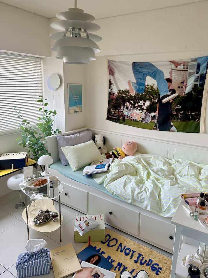 White and natural toned bedroom featuring bed, rug, wall mirror, and greenery with a simple cozy atmosphere