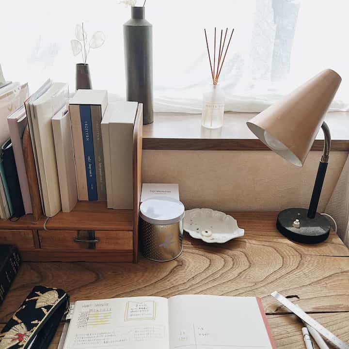 Natural color tone bedroom desk space featuring a wooden desk with books, diffuser, and table lamp creating a cozy atmosphere