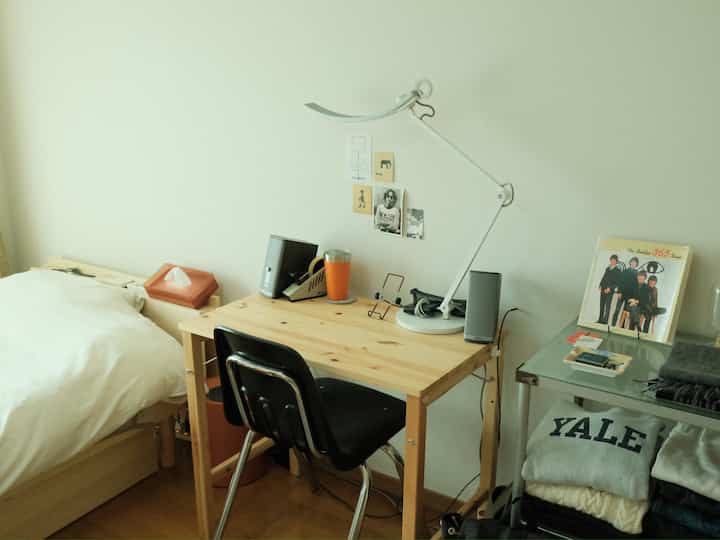 白と茶色のトーンのワンルームホームオフィス、シンプルな机とベッドが配置された落ち着いた空間