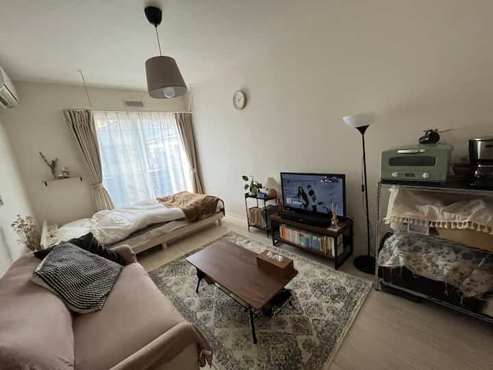 ベージュ色調のワンルーム寝室兼リビング、ソファとコーヒーテーブルが配置された落ち着いた空間