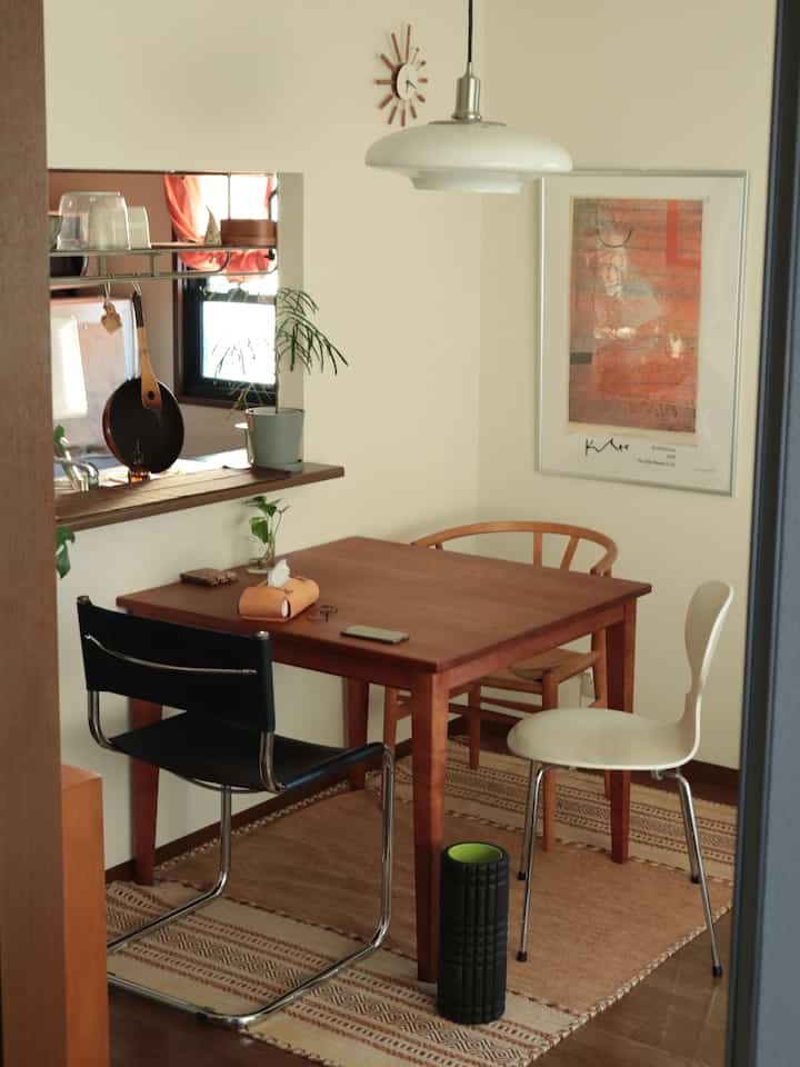 ベージュの壁と木目調の家具が調和するダイニング、テーブルと椅子、ペンダントライトが温かみのある雰囲気を演出しています。