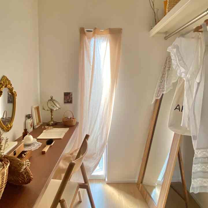 Bright walk-in closet with natural wood tone flooring and furniture, featuring a clothes rack and full-length mirror in a simple setting