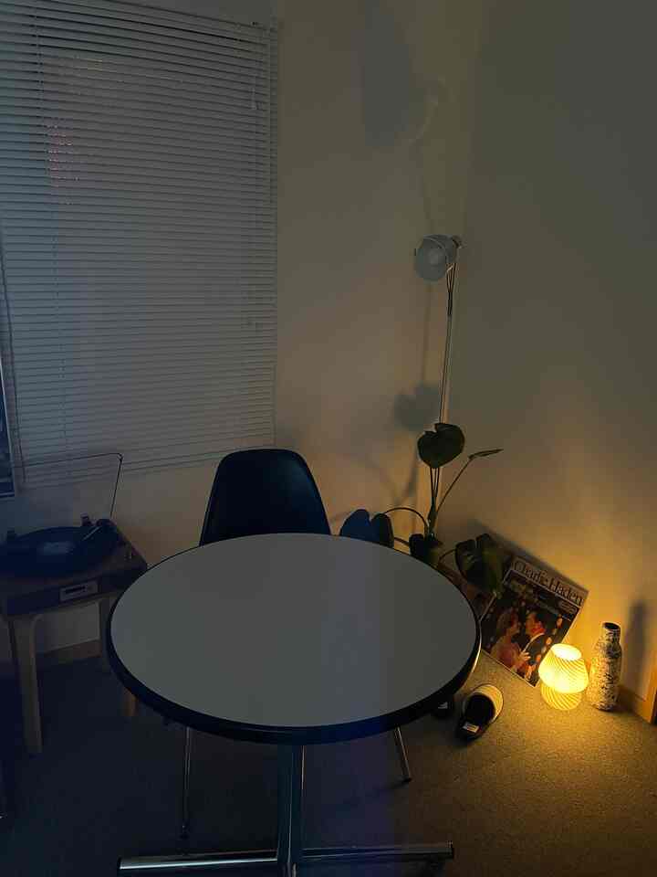 Cozy small living room with white round dining table, black chair, floor lamp in corner and quaint mushroom table lamp glowing warmly in dim light