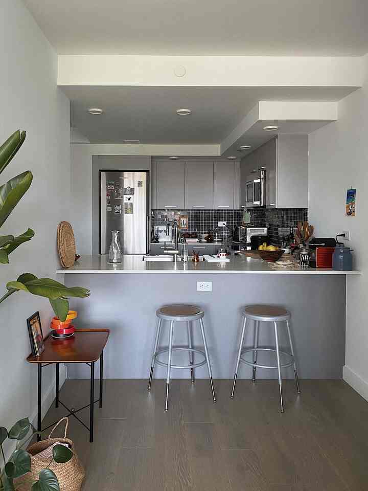 Gray and natural toned kitchen space featuring two silver metal stools, plants, and a modern atmosphere