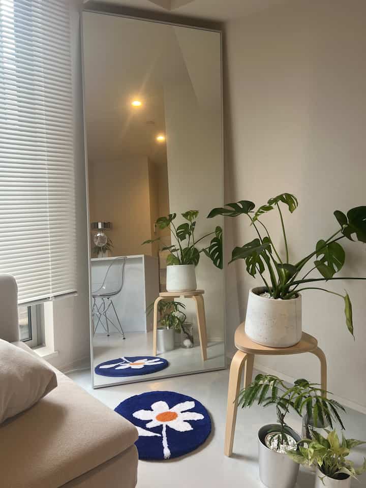 ナチュラルな色調のリビング、ベージュのソファとモンステラの植物、青い花柄のラグが配置された温かみのある空間