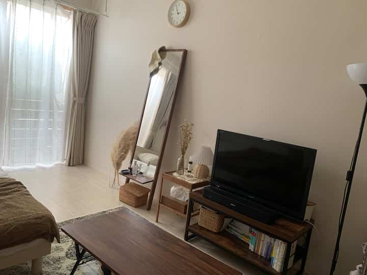 ライトブラウンとホワイトのトーンでまとめられた小さなリビング、テレビ台と全身鏡、木製のコーヒーテーブルが配置された自然な雰囲気のインテリア