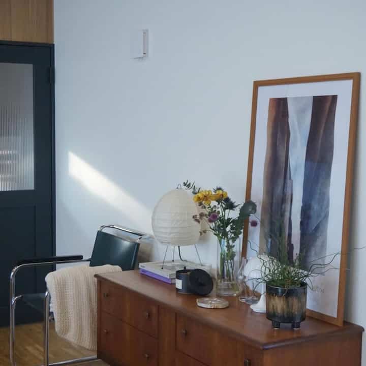 ホワイトの壁とブラウンの木製キャビネット、植物と花瓶、テーブルランプが配置されたナチュラルな印象のリビング