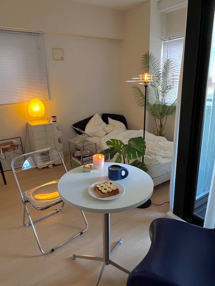 白とナチュラルカラーの寝室、透明な椅子と丸いダイニングテーブルにトーストとコーヒーが置かれた雰囲気のある朝の空間