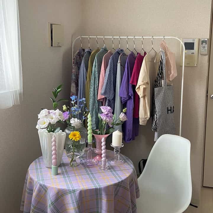 White and beige toned small room featuring white clothes rack, vases, candles on a table with checkered cloth creating cozy atmosphere