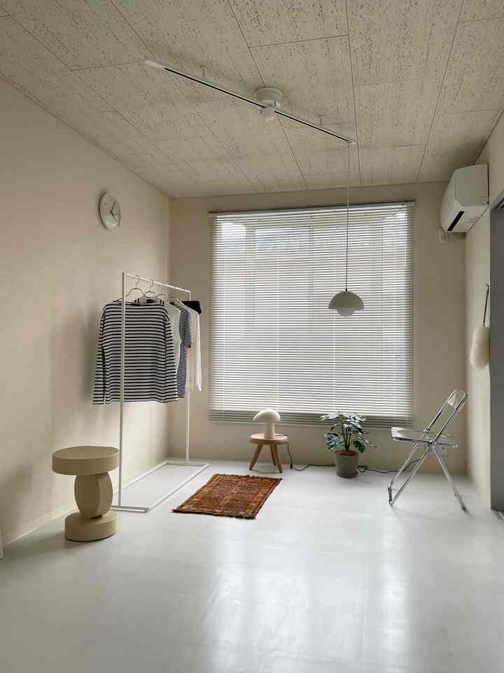 ホワイトとベージュの色調のワンルーム、ミニマルな家具とトライバルラグが配置された清潔感のある空間