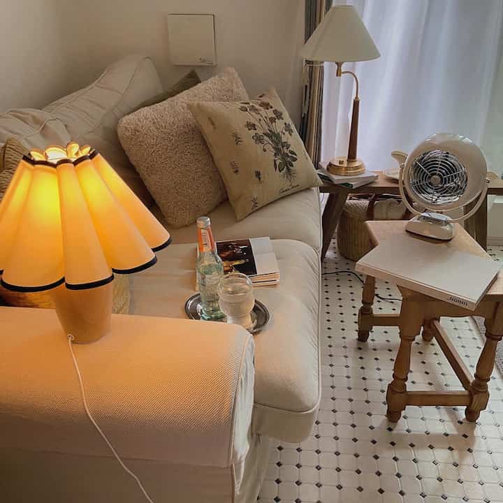 ホワイトとウッドトーンのリビング、クリーム色のソファとヴィンテージ風ランプが配置された温かみのある空間