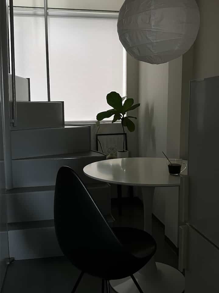 モノトーン調の一人暮らし空間、白い丸いダイニングテーブルと黒い椅子、紙製のペンダントライトが配置されたシンプルなインテリア