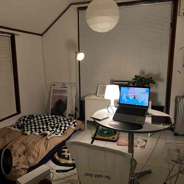 White and brown toned small bedroom featuring pendant light, laptop on round table, bed with blanket, and floor lamp creating cozy ambiance