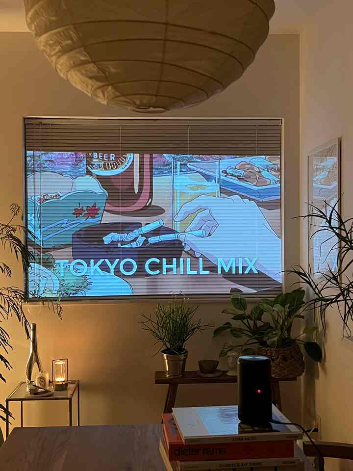 White-walled living room featuring a brown wooden table with Nebula Capsule II projector in center, decorated with plants and books, simple style
