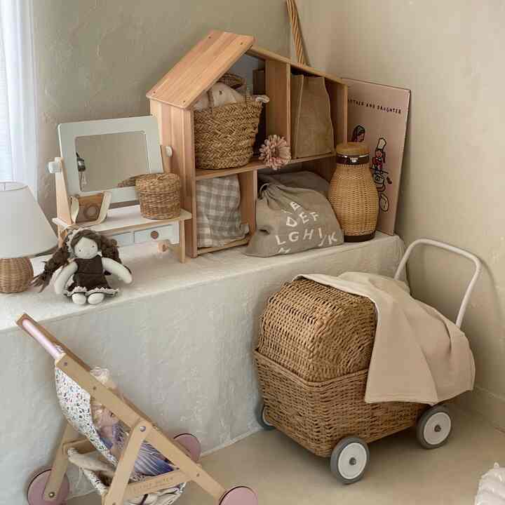 ベージュと木目調の子供スペース、木製の棚とラタンの収納が赤ちゃんと子供のための自然で落ち着いた雰囲気のインテリアを演出