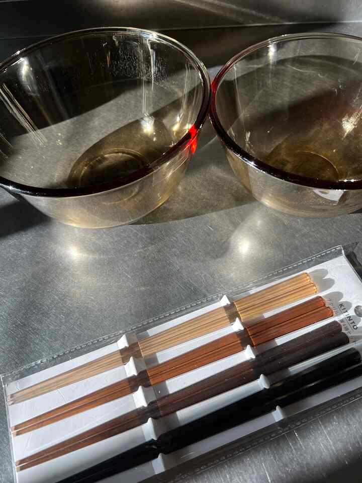 ブラウンの透明なガラスボウルとアクリル製箸セットが金属の上に置かれたキッチン用品の写真