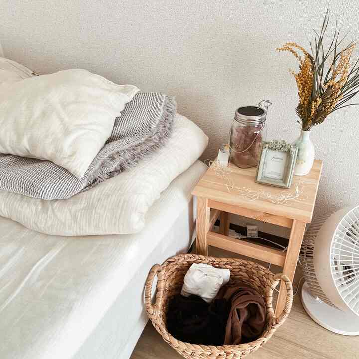 Natural-toned bedroom featuring bed with pillows, wooden stool nightstand, and a woven basket creating a cozy atmosphere